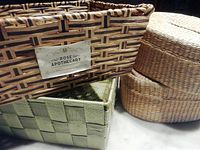 Close-up of four woven baskets: large rectangular Rose Apothecary basket, green square basket, and two round nesting baskets with lids stacked.