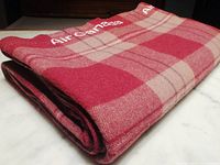 Folded burgundy plaid wool blanket showing 'Air Canada' woven text and plaid pattern.