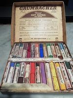 Open box showing two rows of 24 assorted full-length pastels in various colors. Some pastels are broken or worn.