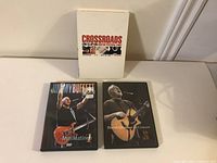 Three music DVDs including Eric Clapton Crossroads Guitar Festival 2013 in white case, David Gilmour in Concert DVD in black case, and Jimmy Buffet Mini Matinee DVD in black case.