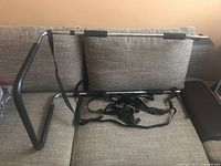 Full view of the metal bed safety rail resting against a grey couch, showing the bent frame, foam padding, and attached straps.