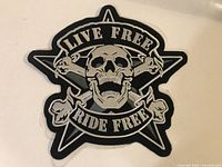 Front view of the black and white embroidered biker patch with skull and crossed bones, showing detail and text.