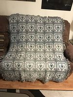 Full view of woven blanket draped on a couch showing front pattern with hearts and floral motifs.