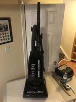 Full view of upright Eureka vacuum cleaner 'The Boss' with handle and hose attached, standing on white table.