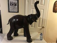 Front side view of the large dark brown elephant figurine with raised trunk and visible tusks next to a water bottle for scale.