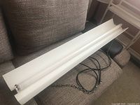 Full view of the white 48 inch grow light fixture with attached 20 inch hanging chains placed on a brown couch.