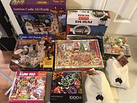 Photo showing the assembled 3D Austrian Castle puzzle in front of the boxed set, Dubai 1000-piece puzzle box, and several flat 1000-piece puzzles including the Blow Pop puzzle and succulent plant photographic puzzle.