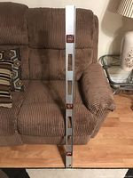 Full view of the 48-inch aluminum level standing vertically against a brown cloth couch, showing length and structure.