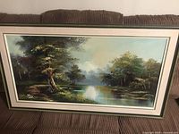 Full view of large framed canvas picture showing tranquil river landscape with trees and sky.