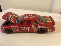 Side view of red Budweiser #25 NASCAR diecast car with opened hood showing detailed engine, placed on beige surface.