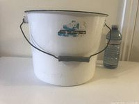 White porcelain enamel bucket with metal handle and plastic grip next to a water bottle for size reference.