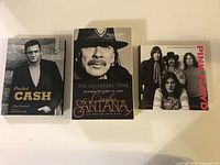 Three music-related books laid out: Pocket Cash, The Universal Tone by Santana, and Pink Floyd Illustrated Biography.