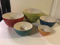 Five ceramic mixing bowls in different sizes and colors arranged on a table, showing shape and color variety