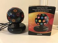 Photo of black spinning disco ball light on a black round base next to its original box, showing product image and multilingual text.