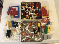 Wide view of various vintage LEGO pieces spread on a surface and laid out around the open tin container full of bricks.