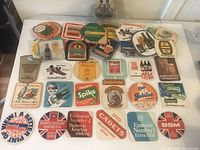 Photo showing a large assortment of vintage bar drink coasters laid out on a table, featuring multiple brands and colorful graphics.