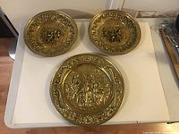 Three brass wall plates arranged on a white surface, showing variety of sizes and embossed designs