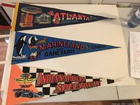 Photo showing three vintage pennants laid flat: Atlanta Georgia, Marineland and Game Farm Canada, and Indianapolis Speedway.