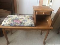 Full view of vintage wooden telephone table showing side profile with drawer and upholstered floral seat.