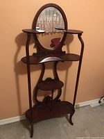 Front view of dark wooden hall stand with oval mirror and multiple shelves against beige wall.