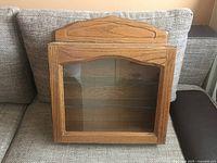 Front view of wooden display cabinet with glass door closed, showing wood grain finish and glass shelves inside.