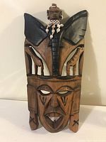 Front view of hand-carved wooden tribal mask with face, elephant, giraffes, and figurine with beaded necklace.