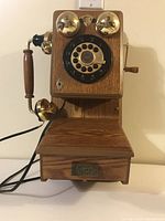 Front view showing wooden body, brass bells, and rotary dial with numeric and alphabetic characters.