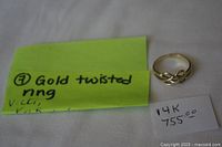 Ring and green handwritten note reading "Gold twisted ring" plus small card marked "14K 755.00" on white background.