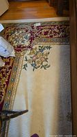 Corner of rug showing burgundy scrolling border with floral motifs and cream field