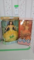 Two boxed Barbie dolls, left is Beauty and the Beast Belle in yellow dress, right is Party Pink Barbie in peach dress