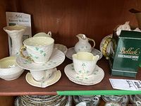 Shelf display of multiple Belleek Shamrock pattern items including stacked cups and saucers, sugar bowl, creamer, vase, teapot and branded box