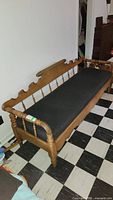 Angled front view of wooden bench with black cushion