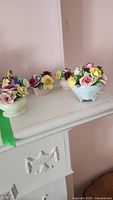 Four small bone china flower arrangements grouped on a white mantel, visible colors pink, purple, yellow, and white.