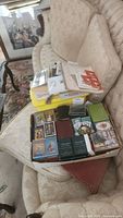 Several boxes of playing cards arranged on a beige sofa including collectible and themed decks.