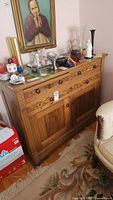 Front view of vintage solid wood buffet with various decorative items on top and a framed portrait hanging behind it.