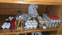 Shelf with multiple packs of white tealight candles, some loose and some in plastic trays, plus a box of red floating candles and several packs of battery operated tealights.