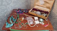 Wide view of assorted jewelry on wooden table showing necklaces, bracelets, brooches, and vintage jewelry case.