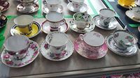 Full view of eight assorted cups and saucers arranged on flat surface showing varied floral and decorative styles