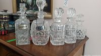Wide view of five crystal decanters on wood surface with floral painting background