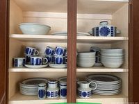 Overall view of dishes on cabinet shelves showing plates, bowls, cups, saucers and serving pieces.