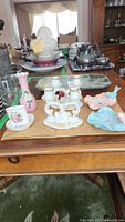 Set of porcelain candle holder, ceramic bird dishes, glass mirror tray, and silver-plated tea set on wooden table.