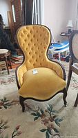 Front view of yellow upholstered fireside chair with tufted back and wooden frame on a floral rug.