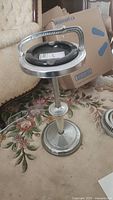 Full view of metal floor ashtray with circular base and glass ashtray insert at the top showing black glass inside metal holder.