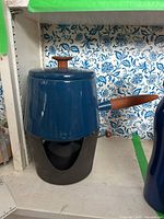 Blue enamel fondue pot with wooden handle on black burner base against patterned background