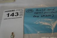 Photo of the gold and opal pendant placed on white paper with category labels, showing the size and shape of the pendant.