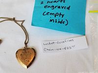 Gold heart-shaped locket pendant and chain laid flat on white fabric