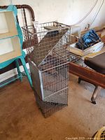 Side view of tall rectangular live animal trap made of metal wire mesh with trigger plate and spring door