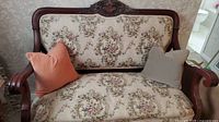 Front view of wood frame loveseat with beige floral upholstery and two accent cushions (orange, beige)