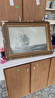 Full view of framed painting showing a tall ship sailing on ocean, frame visible with notable damage.