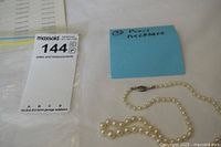 Photo showing pearl necklace with a visible sterling silver filigree clasp laid on a white surface with a blue sticky note identifying it as 'Pearl necklace'.
